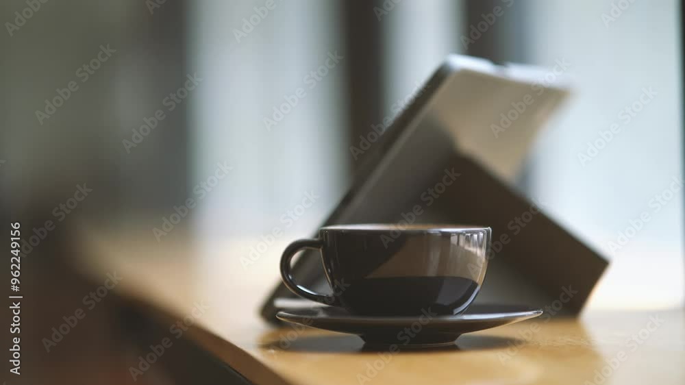 Morning Coffee Break: A cup of coffee and a tablet rest on a wooden table near a window, capturing the essence of a quiet and serene moment. Morning Coffee Break: A cup of coffee and a tablet rest on a wooden table near a window, capturing the essence of a quiet and serene moment.