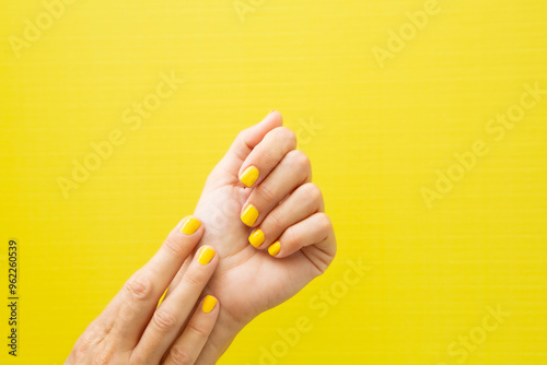Woman's hands with yellow painted nails on a yellow background