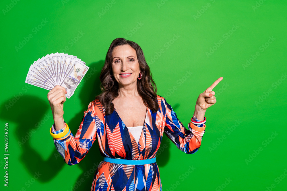 Photo of cheerful pretty lady dressed print outfiit rising money fan pointing empty space isolated green color background Photo of cheerful pretty lady dressed print outfiit rising money fan pointing empty space isolated green color background