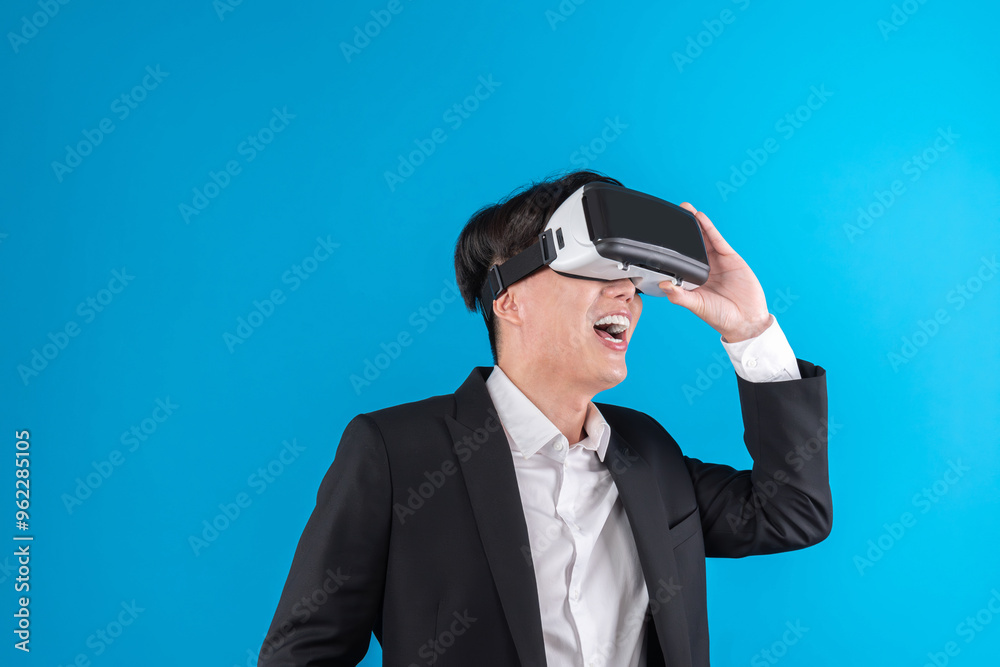 Smiling Asian businessman looking thorough VR connecting to business world report in futuristic metaverse, analyzing innovation technology ads in virtual reality isolated blue copyspace. Contrivance. Smiling Asian businessman looking thorough VR connecting to business world report in futuristic metaverse, analyzing innovation technology ads in virtual reality isolated blue copyspace. Contrivance.