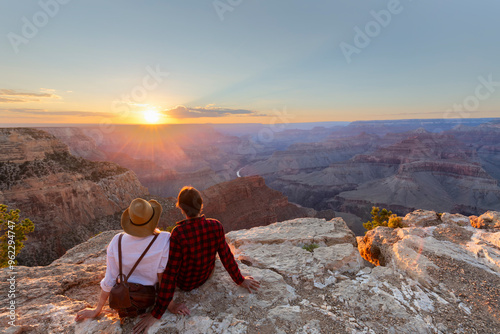 A man and a woman sit at the edge of the Grand Canyon at sunset minutes