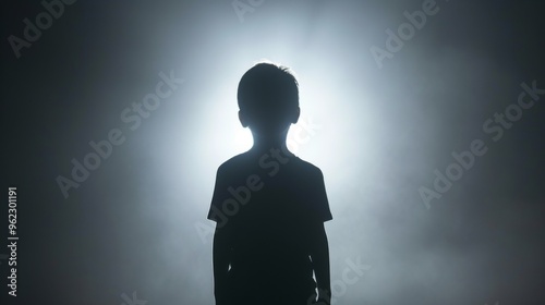 A powerful silhouette of a child standing against a bright, misty background, creating a dramatic and mysterious effect. The light halo enhances the focus on the child's outline, evoking themes of