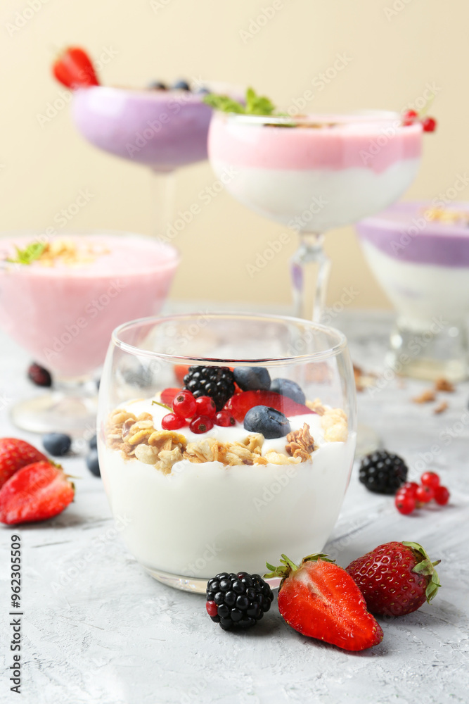 Different tasty yogurts with fresh berries and granola in glass dishware on gray textured table, closeup Different tasty yogurts with fresh berries and granola in glass dishware on gray textured table, closeup