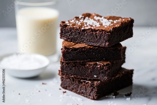 A stack of fudgy vegan chocolate brownies, topped with a sprinkle of sea salt and a side of almond milk