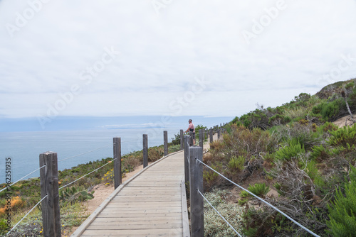 Man standing on the boardwalk at Pt. Dume Natural Preserve overlooking the Pacific Ocean, California photo