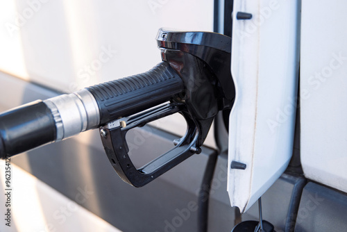 Fototapeta Naklejka Na Ścianę i Meble -  Closeup of a fuel nozzle in the car tank. Process of refilling a white transporter bus at a gas station. Refueling pistol inserted into a vehicle at a gas station. Copy space