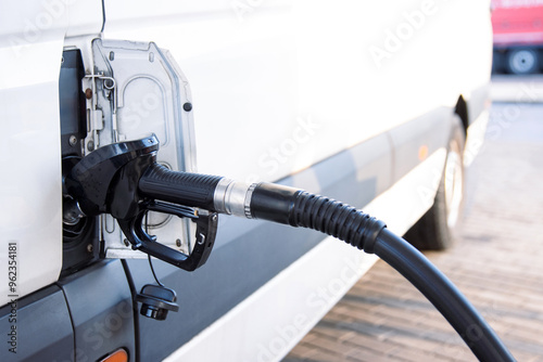 Fototapeta Naklejka Na Ścianę i Meble -  Closeup of a fuel nozzle in the car tank. Process of refilling a white transporter bus at a gas station. Refueling pistol inserted into a vehicle at a gas station. Copy space