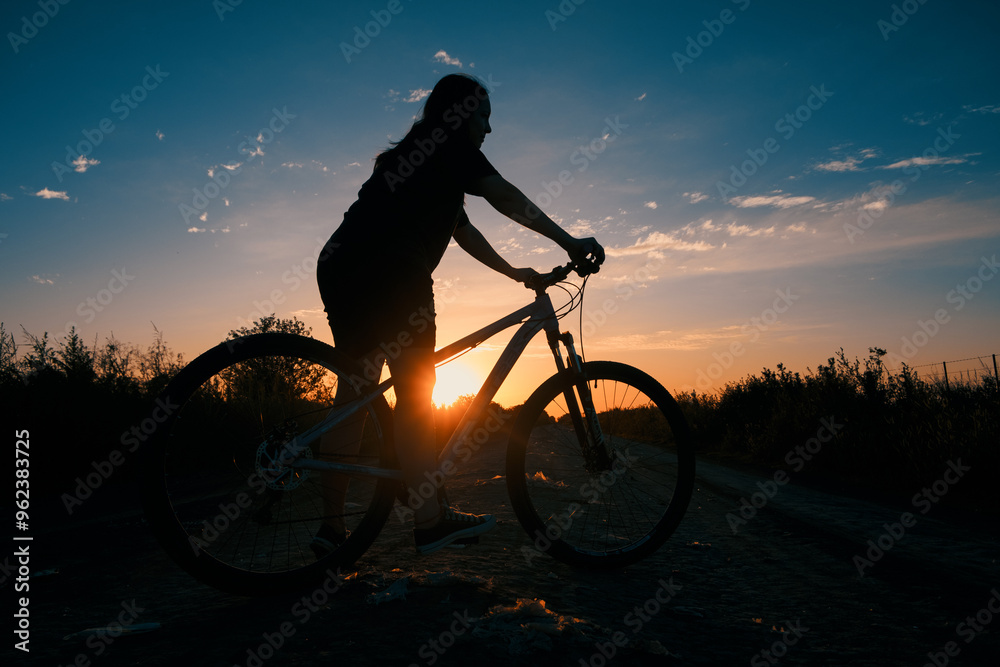 Naklejka premium Silueta de chica en bicicleta durante el atardecer
