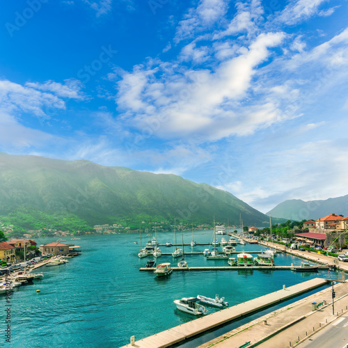 beautiful Kotor bay in Montenegro, Balkans. Sea landscape of turquoise sea gulf with urban embarkment, touristic boats and yacht and scenic green mountains with blue sky with nice cloud on background