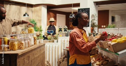 African american client putting organic produce in a paper bag, buying natural ethically sourced pesticides free vegetables. Woman choosing homegrown goods, sustainable lifestyle. Camera 2. photo