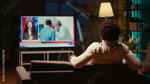 Man watching TV late at night, informing himself on latest news by watching reporter cover different subjects. Person relaxing by looking at smart TV in dimly lit apartment photo