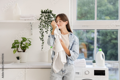 Young woman smelling clean towel in laundry room photo