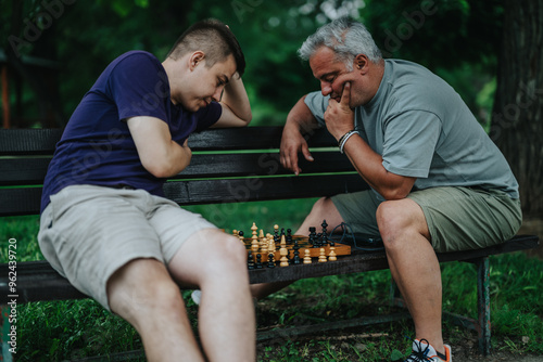 Tableau sur toile A father and son deeply focused on a chess game while sitting on a park bench