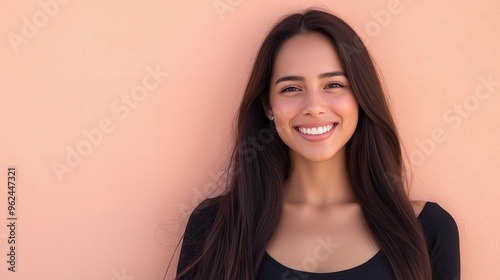 A young woman with long dark hair and a white smile stands against a pink wall.