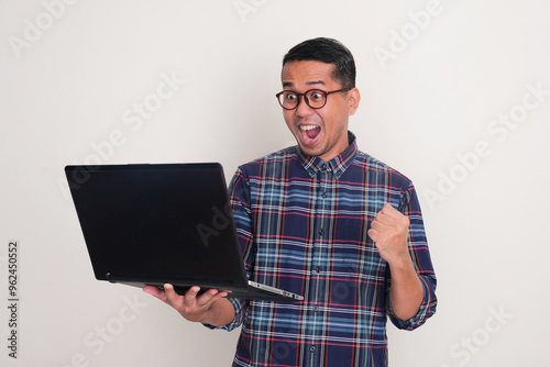 A man clenched fist showing excited when looking at the laptop that he hold photo