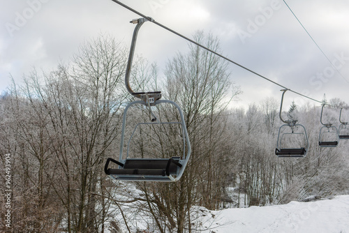 Ski lift, T-bar transports people to the top of a snowy mountain. Lots of coniferous trees and snow around. Cloudy, cold weather. Skiing and snowboarding. Vyshka, Zakarpattia region, resort 