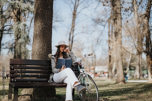 A fashionable young lady is immersed in a book on a bench in a vibrant city park, her bicycle parked next to her.