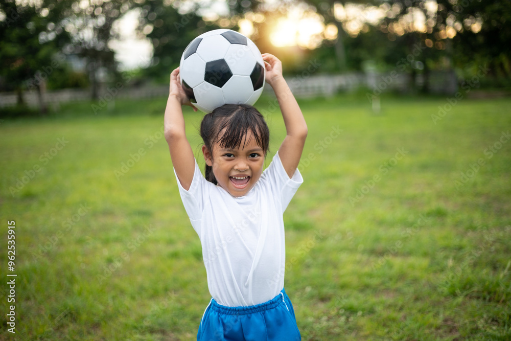 A young girl is holding a soccer ball in a park. She is smiling and she is enjoying herself A young girl is holding a soccer ball in a park. She is smiling and she is enjoying herself