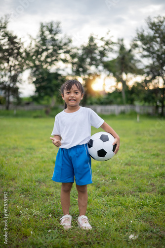 A young girl is holding a soccer ball in a park. She is smiling and she is enjoying herself