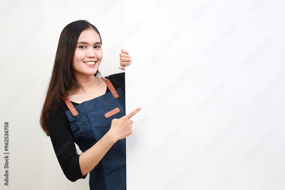 Happy Asian woman in apron pointing something on white advertisement board on white background Happy Asian woman in apron pointing something on white advertisement board on white background