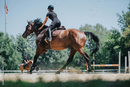 A woman in black riding attire enjoys horseback riding in an outdoor arena on a sunny day, showcasing equestrian skills and passion.