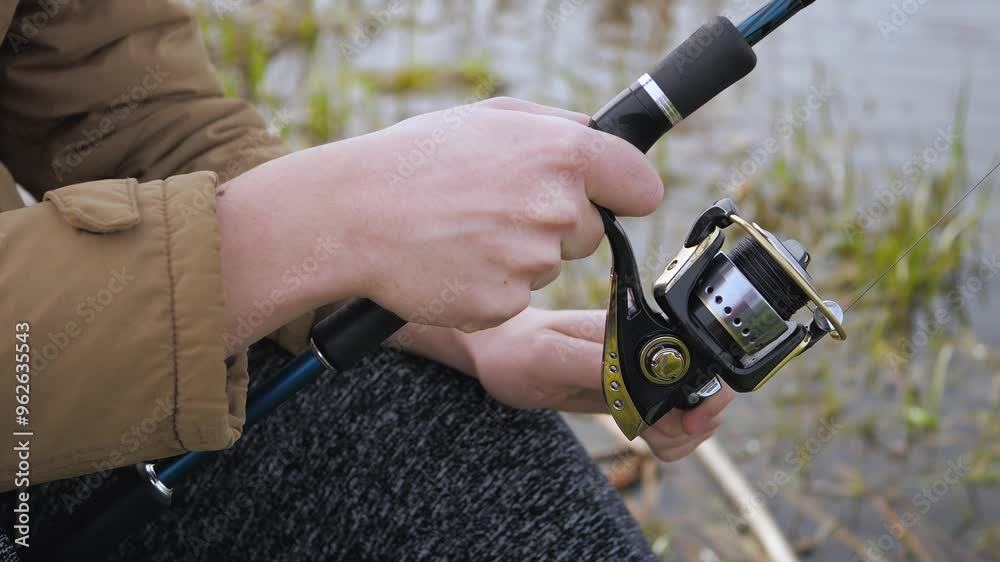 Fisherman's hand winding the fishing line onto the reel of a spinning rod. Summer fishing. Slow motion.