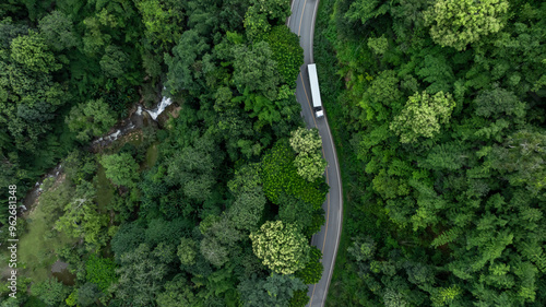 Fototapeta Naklejka Na Ścianę i Meble -  Aerial view semi truck with cargo trailer on road curve with green tree forest, Transportation logistic cargo background, Semi truck trailer on asphalt forest road in green tree forest.