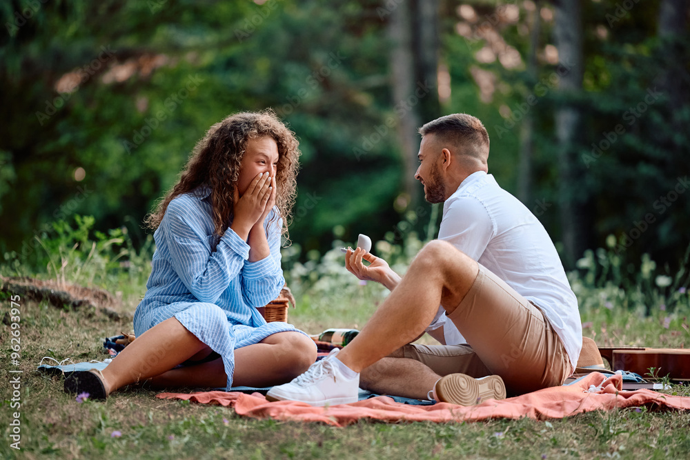 Fototapeta premium Young woman feeling surprised while her boyfriend is proposing her on picnic.