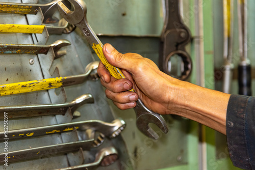 A board filled with hanging wrenches in a ship’s workshop, as a crew member from the engine department reaches for one. Practical tools and skilled hands keep a merchant vessels running smoothly. photo