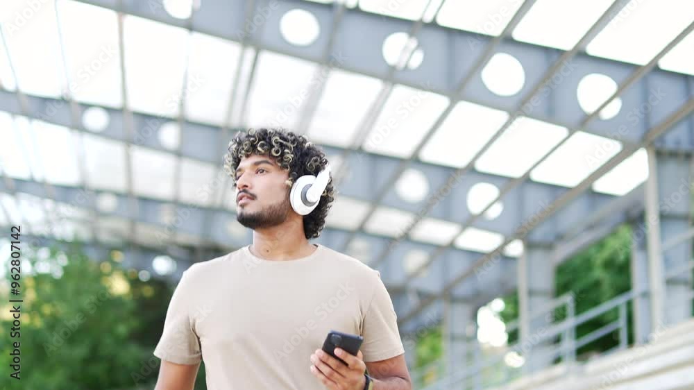 Focused male in headphones using smartphone walking in outdoor urban environment. Young man enjoying music on phone modern lifestyle and technology leisure activity and listening music Focused male in headphones using smartphone walking in outdoor urban environment. Young man enjoying music on phone modern lifestyle and technology leisure activity and listening music