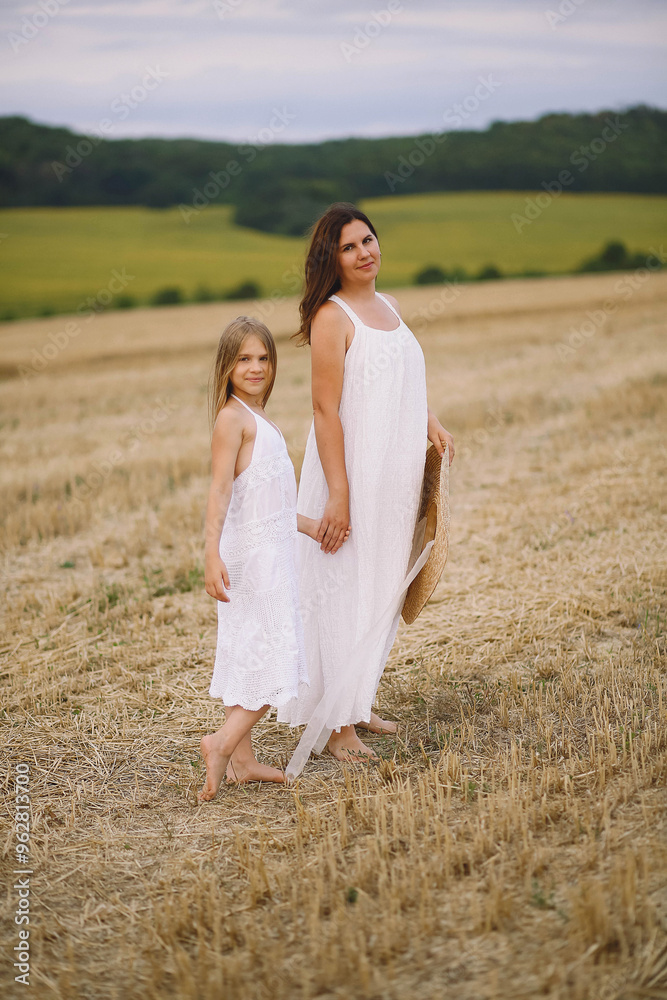 Happy mother and daughter in summer dresses walking on the field Happy mother and daughter in summer dresses walking on the field