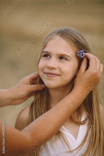 Mother holding wild flower near hair of her daughter outdoor