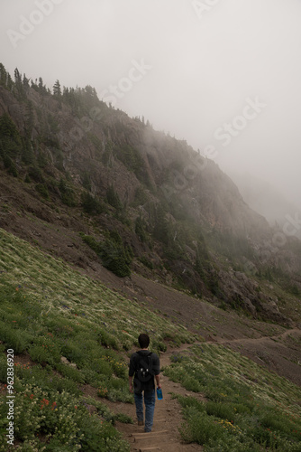 Man walking down mountainside hiking trail with fog