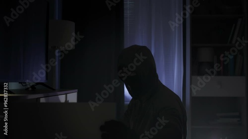 robbery, a thief in black clothes and a balaclava rummages through other people's things in search of valuables at night in an apartment