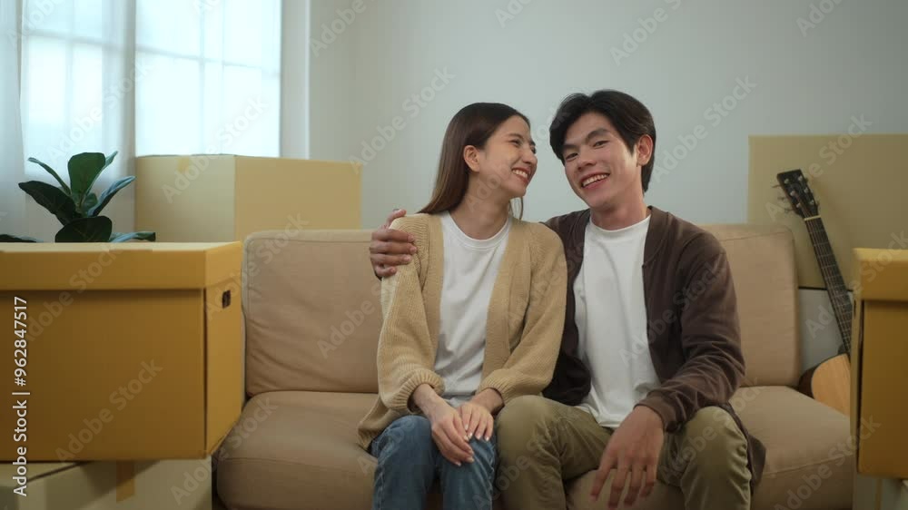 young asian cheerful couple sitting on sofa and smiling to each other after moving to new house with pile of cardboard boxes, relocating real estate apartment concept.
young asian cheerful couple sitting on sofa and smiling to each other after moving to new house with pile of cardboard boxes, relocating real estate apartment concept.