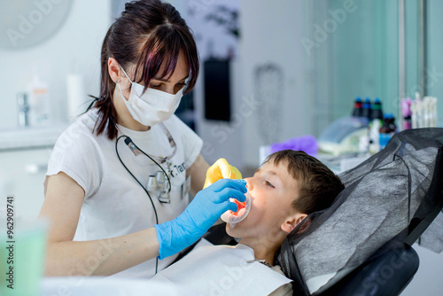Картината върху платно Paediatric dentist putting a cheek retractor on child patient before dental trea