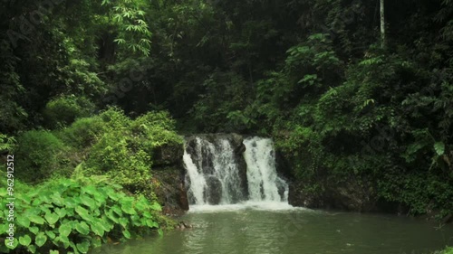 Drone view beautiful scenery of waterfall in tropical rainforest during rainy season. Water stream flowing over the cascade through lush foliage vegetation in the jungle. Wild nature background.