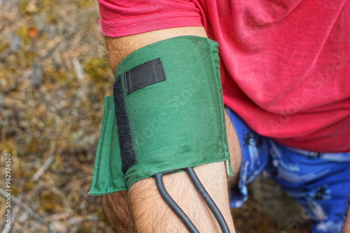 Fotografía green medical rubber cuff with black hoses applied to patient's arm in red t-shi