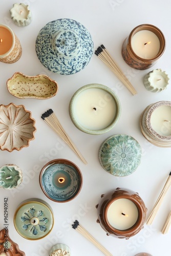 A flat lay of various scented candles with decorative holders and matches arranged aesthetically