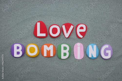 Love bombing, an attempt to influence a person by demonstrations of attention and affection, creative text composed with hand painted multi colored stone letters over green sand
