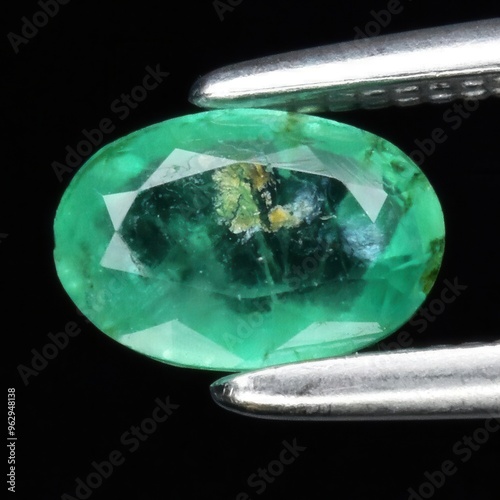 Captivating Close-Up of a Pristine Green Emerald Gemstone Held by Precision Tweezers on a Dark Background photo