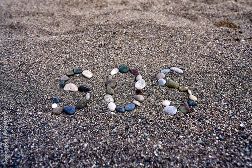 A serene beach scene showcases an SOS signal artfully created from a variety of colorful stones on the sandy ground