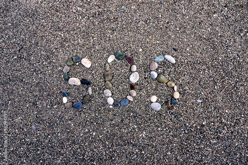 A serene beach scene showcases an SOS signal artfully created from a variety of colorful stones on the sandy ground