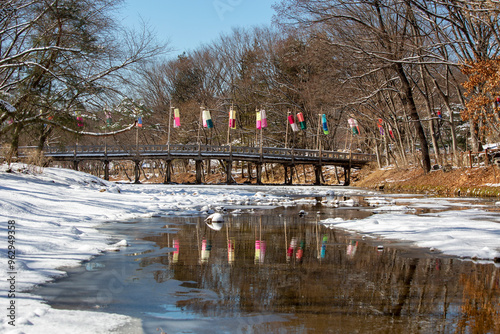 Korean Folk Village, Yongin-si, Gyeonggi-do, South Korea - February 04, 2021: Brook with ice and snow against a wood bridge with traditional Korean lanterns photo