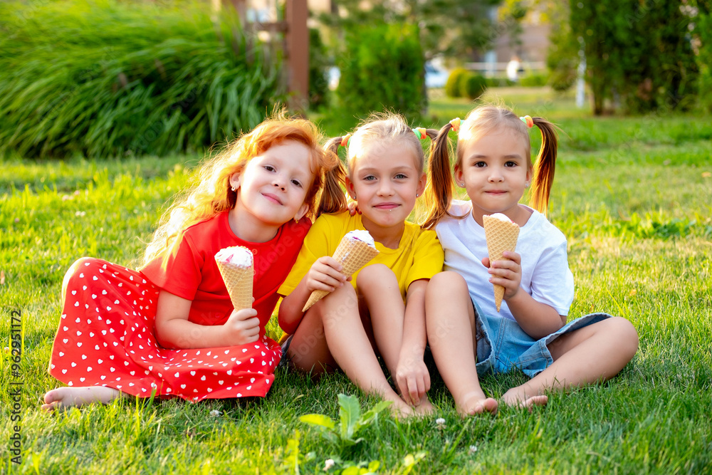 Fototapeta premium happy children eating ice cream in the summer on the green lawn in the park, a bright summer photo of children's holidays, three baby girls laughing and having fun in the summer