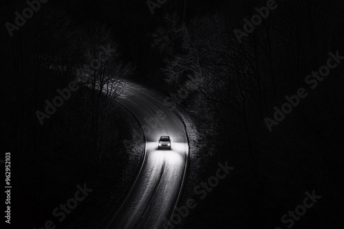 A car navigating a winding road illuminated by headlights on a dark night surrounded by trees photo