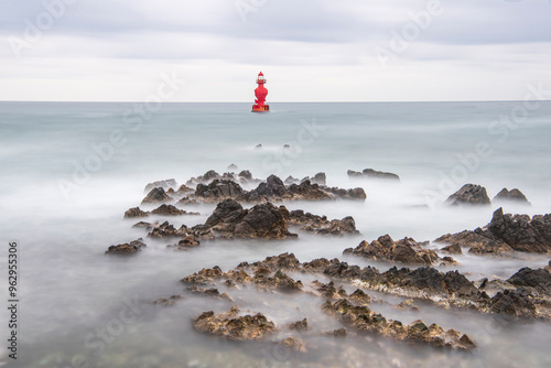 Long exposure of wave on sea rocks against sea horizon and a red lighthose near Eodal Beach at Donghae-si, South Korea photo