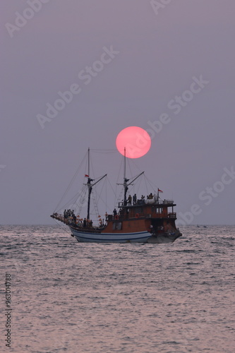 A phinisi boat sails against a beautiful sunset