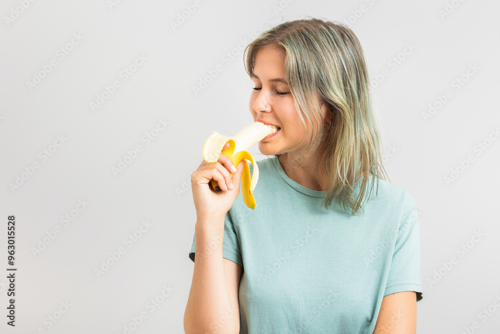 Young cheerful woman eating a banana. Isolated on gray background Young cheerful woman eating a banana. Isolated on gray background