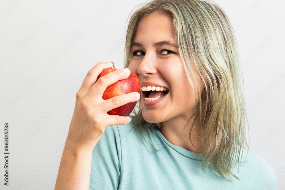 Cute young woman eating a red apple. Isolated on gray background Cute young woman eating a red apple. Isolated on gray background